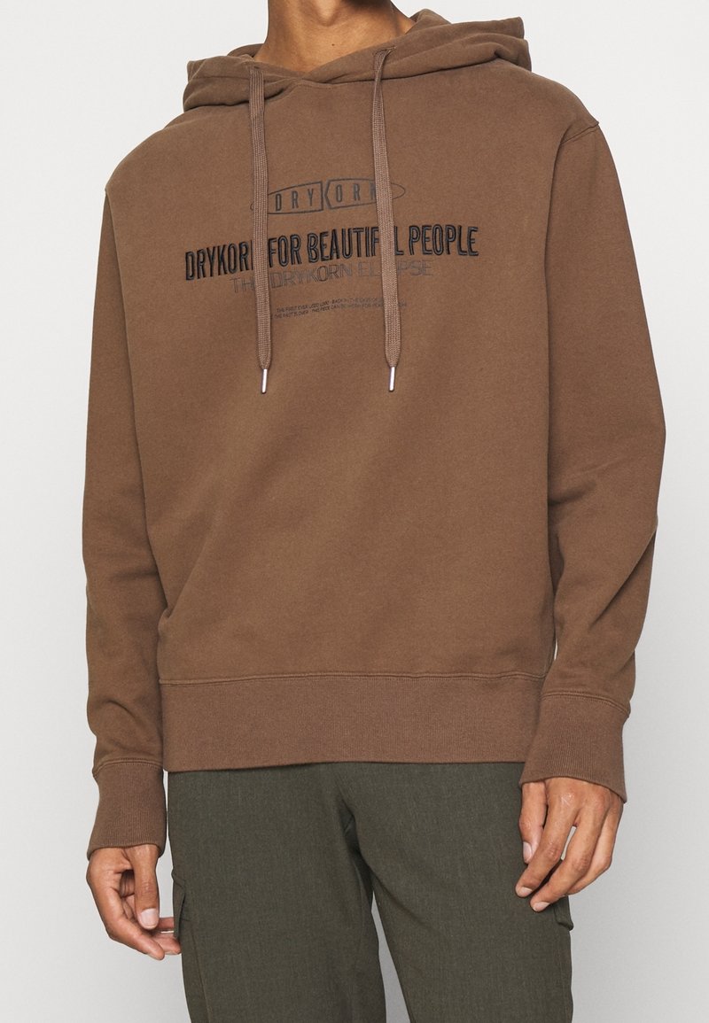 Sudadera con capucha marrón hecha de una tela suave, que presenta un gráfico frontal en texto negro. Incluye cordones y puños y dobladillo acanalados.