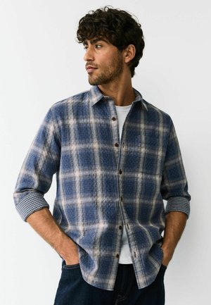 Blue and white checkered flannel shirt with a buttoned front and rolled-up sleeves, featuring a textured pattern and brown buttons.