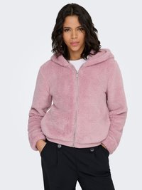 Veste à capuche rose clair, duveteuse, avec une fermeture éclair sur le devant, des poignets et un ourlet côtelés. Comprend une capuche doublée et des poches, portée sur un haut blanc.