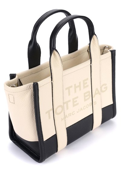 Bolsa de tote em pele com um corpo bege e detalhes pretos. Texto "A BOLSA TOTE" e "MARC JACOBS" impressos em uma cor clara na lateral.