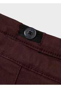 Burgundia püksid lähedalt, musta kangast vöökoha ja nelja auguga ringikujulise metallnupuga. Nähtav tekstuuriga kangas.