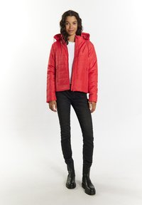 Giacca a vento rossa con zip frontale, cappuccio e design trapuntato. Indossata con un maglione bianco, jeans neri e stivali neri alla caviglia.
