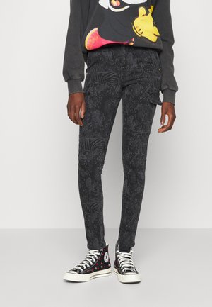 Personne portant un pantalon cargo noir skinny avec des motifs zébrés subtils, un sweat-shirt graphique, et des baskets montantes noires avec des points rouges et blancs.