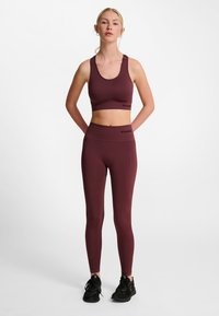 Completo activewear color bordeaux composto da un top corto e leggings a vita alta realizzati in tessuto elasticizzato e traspirante con una texture liscia.