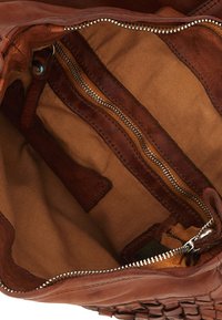 Interno di una borsa a tracolla in pelle marrone che mostra la fodera in tessuto, una tasca interna con zip e una cerniera metallica parzialmente aperta.