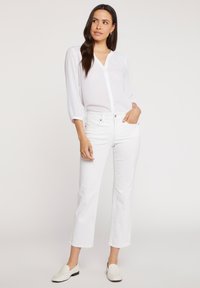 Blusa blanca de manga larga con escote en V y cierre de botones, combinada con unos vaqueros blancos cropped y zapatos slip-on blancos. Textura de tela suave.