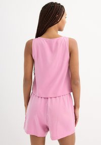 Top sin mangas de color rosa con un corte relajado, combinado con pantalones cortos a juego. Tejido ligero y detalle de cinturilla elástica. Textura suave.