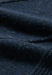 Nahaufnahme eines dunkelblauen Wollstoffs mit einem strukturierten Strickmuster und kleinen helleren Farbflecken.