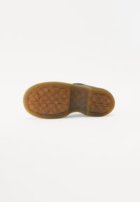 Sole di scarpa in gomma con un motivo testurizzato e scanalato. Le transizioni di colore vanno dal marrone a una tonalità più chiara con forme circolari e rettangolari.