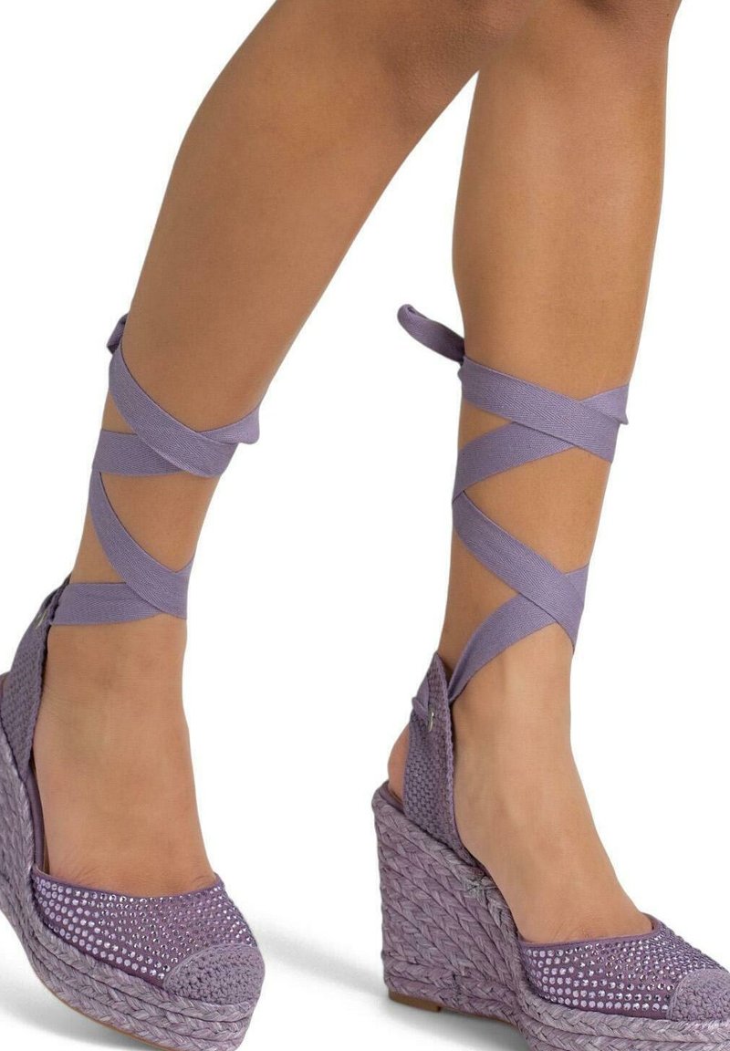 Espadrille à talon en forme de coin violet, avec une texture tissée, des accents en strass sur le bout, et des sangles en ruban entrecroisées autour de la cheville.