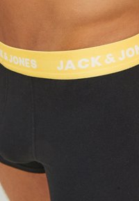 Schwarze Baumwoll-Boxershorts mit einem gelben Elastikbund, der das weiße Logo "JACK & JONES" trägt. Weiche Textur und enganliegendes Design.