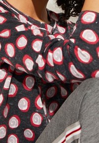 Langarmhemd aus dunkelgrauem Stoff mit rot-weißer Spiralpunktmusterung, mit leicht abgerundetem Halsausschnitt und weicher Textur.