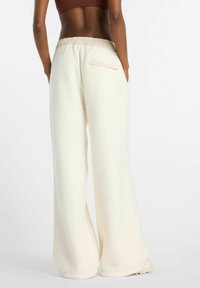 Wijde broekspijpen van zachte, crèmekleurige stof met een gestructureerde afwerking. Voorzien van een elastische tailleband en een enkele achterzak met een minimalistisch ontwerp.