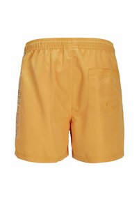Bañadores amarillos con cinturilla elástica, que cuentan con un bolsillo en la parte posterior y texto blanco de logo en el lado izquierdo. Textura suave y bordes rematados.