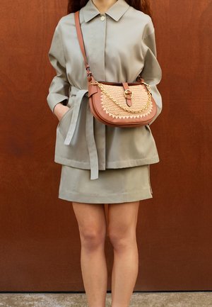 Cappotto grigio chiaro a maniche lunghe con vita alta, abbinato a una gonna coordinata. La borsa beige presenta dettagli intrecciati e una catenina dorata.
