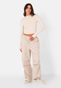 Beige langemouwen top met rits aan de voorkant en slim fit, gecombineerd met loszittende beige cargobroek met zijzakken en elastische boorden.