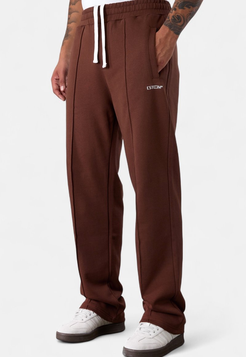 Braune Jogginghosen mit weißem Kordelzug, Seitentaschen und subtilen Logodetails. Glatte Textur mit kontrastierenden seitlichen Paspeln.