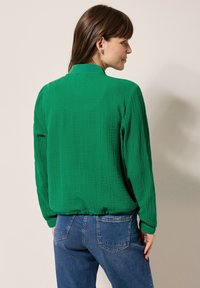 Groene, gestructureerde blouse met een kraag, lange mouwen, elastische zoom en een relaxte pasvorm, gecombineerd met blauwe denim jeans.