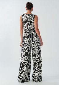 Zwart-wit zebraprint jumpsuit met mouwloos topje, open rug en broek met wijde pijpen. Gemaakt van lichte stof met een vloeiend ontwerp.