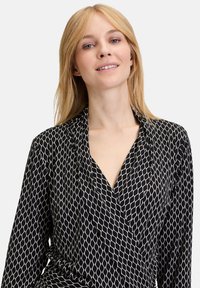 Svart inslagblus med ett diamantmönster i kräm, med djup halsringning och långa ärmar, tillverkad av ett mjukt, lätt tyg.