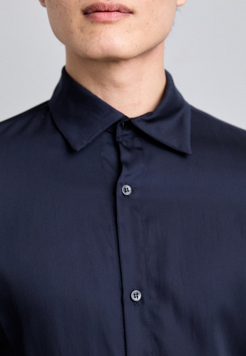 Navy button-up shirt featuring a classic collar, smooth texture, and subtle sheen. Six buttons down the front, no visible patterns or accents.