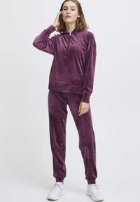 Velvet trainingspak in diep paars, met een doorritsbare hoodie en bijpassende broek met elastische manchetten. Zachte, gestructureerde stof, relaxte pasvorm.