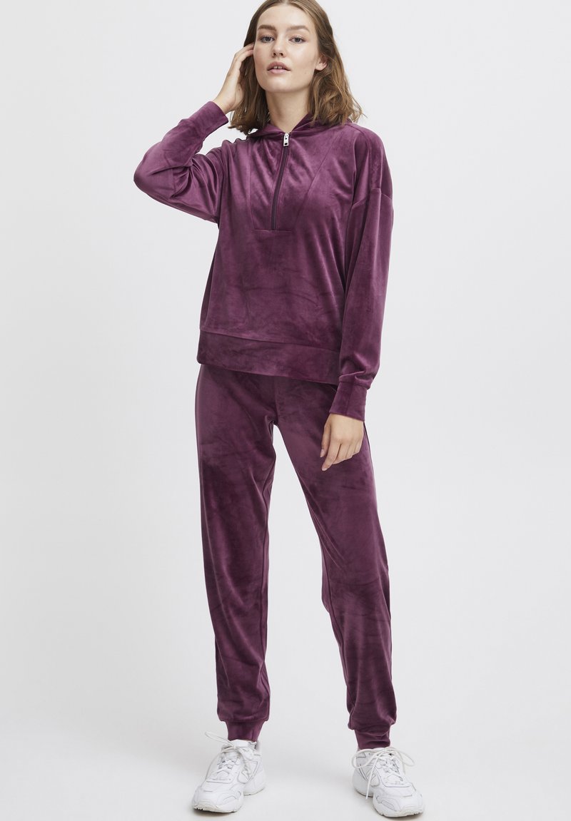 Velvet trainingspak in diep paars, met een doorritsbare hoodie en bijpassende broek met elastische manchetten. Zachte, gestructureerde stof, relaxte pasvorm.