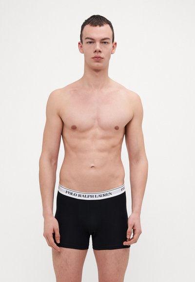 Crne bokserice s bijelim pojasom na kojem piše "POLO RALPH LAUREN." Tkanina izgleda glatko, a dizajn je prilagođen s srednjim razrezom.