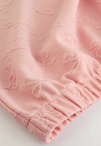 Helles pinkes Kleidungsstück aus strukturiertem Stoff mit dezenten erhabenen Mustern, gerafften Kanten und einem gerippten Saum für Elastizität.