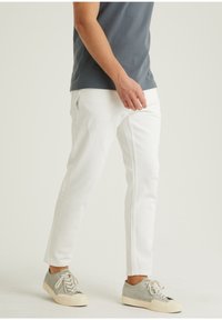 Pantalones de denim blancos con un corte ajustado, con un ligero desgaste en la parte frontal, combinados con zapatillas grises y una camisa de manga corta azul.