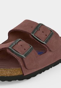Κοντινό πλάνο καφέ σάνδαλου Birkenstock με δύο ρυθμιζόμενες μεταλλικές αγκράφες και φελλό πάτο σε λευκό φόντο.