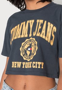Šedé zkrácené tričko s textem "TOMMY JEANS" a žlutým logem glóbu. Má krátké rukávy a design s kulatým výstřihem.