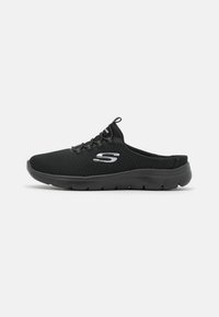 Svart slip-on träningsskor i meshmaterial med texturerad yta. Funktioner inkluderar elastiska snören och en vadderad sula. Silverlogotyp på sidan.