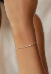 Pulsera de plata con formas ovaladas interconectadas y una única bola blanca. El diseño es delicado y minimalista, complementando la muñeca.