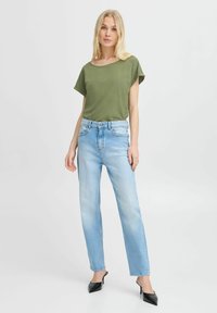 Top verde de manga corta, jeans de pierna recta en azul claro y tacones negros de punta. Tejido suave, ajuste casual, sin patrones ni acentos visibles.