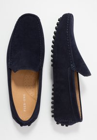 Marinblå ruskinds loafers med gummidutter på sålen, med stikninger og design med rund tå. Flad, slip-on stil.