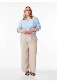Camicia a righe blu chiaro con maniche arrotolate, abbinata a pantaloni larghi beige. L'outfit presenta una vestibilità comoda e sandali semplici.