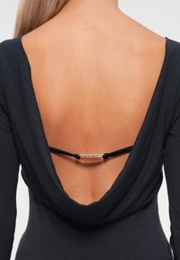 Czarny top z drapowaniem, z głębokim dekoltem w kształcie litery V na plecach, ozdobiony kontrastującymi srebrnymi detalami połączonymi czarnymi sznurkami.