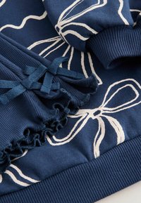 Mörkblå sweatshirt i tyg med vita blommönster, texturerade volanger och ribbade detaljer vid fåll och ärmslut.