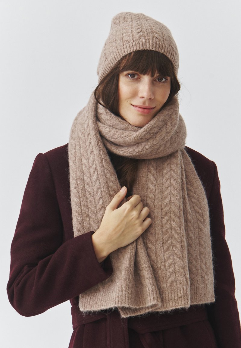 Gebreide wol muts en bijpassende sjaal in zacht beige, met een getextureerd rib- en kabelpatroon. Warm, comfortabel en lichtgewicht materiaal.