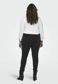 Black skinny jeans with a smooth texture, two back pockets, and a high waistband, paired with a white long-sleeve blouse.
