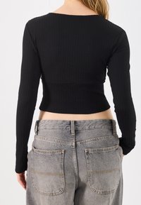 Person wearing a fitted black ribbed long-sleeve top and high-waisted faded gray jeans, viewed from the back.