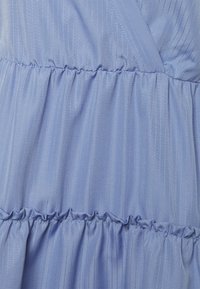 Abito azzurro chiaro con tessuto testurizzato a righe verticali, tiers a volant e arricciatura elastica in vita.
