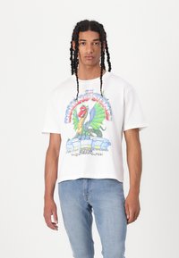 White cotton t-shirt featuring a colorful Rolling Stones graphic with a dragon and concert scene. Short sleeves, relaxed fit, minimal texture.