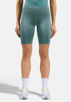 Türkisfarbene Radsportshorts mit hoher Taille und glatter Textur, mit einem Logo an der Seite. Getragen mit weißen Socken und hellblauen Laufschuhen.