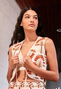 Veste blanche avec broderie florale orange, design court, soutien-gorge à bretelles avec bordure en dentelle en dessous, texture lisse et détails subtils.