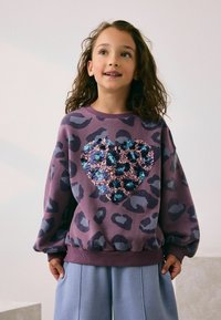 Lilla sweater med sort og grå leopardprint, med et hjerte lavet af pailletter i nuancer af blå og pink, ribbede manchetter og kant.