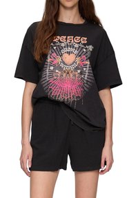 T-shirt noire surdimensionnée avec un design graphique coloré comprenant du texte et un motif floral, associée à un short noir ample.