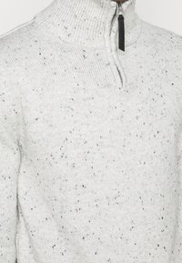 Maglione grigio chiaro con accenti blu maculati, colletto alto e chiusura a metà zip. Realizzato in tessuto a maglia textrurato.
