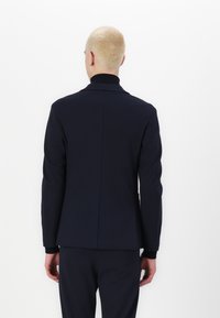Navy blue blazer with structured shoulders, a smooth texture, and a tailored fit. Features a high collar and seamless back design.